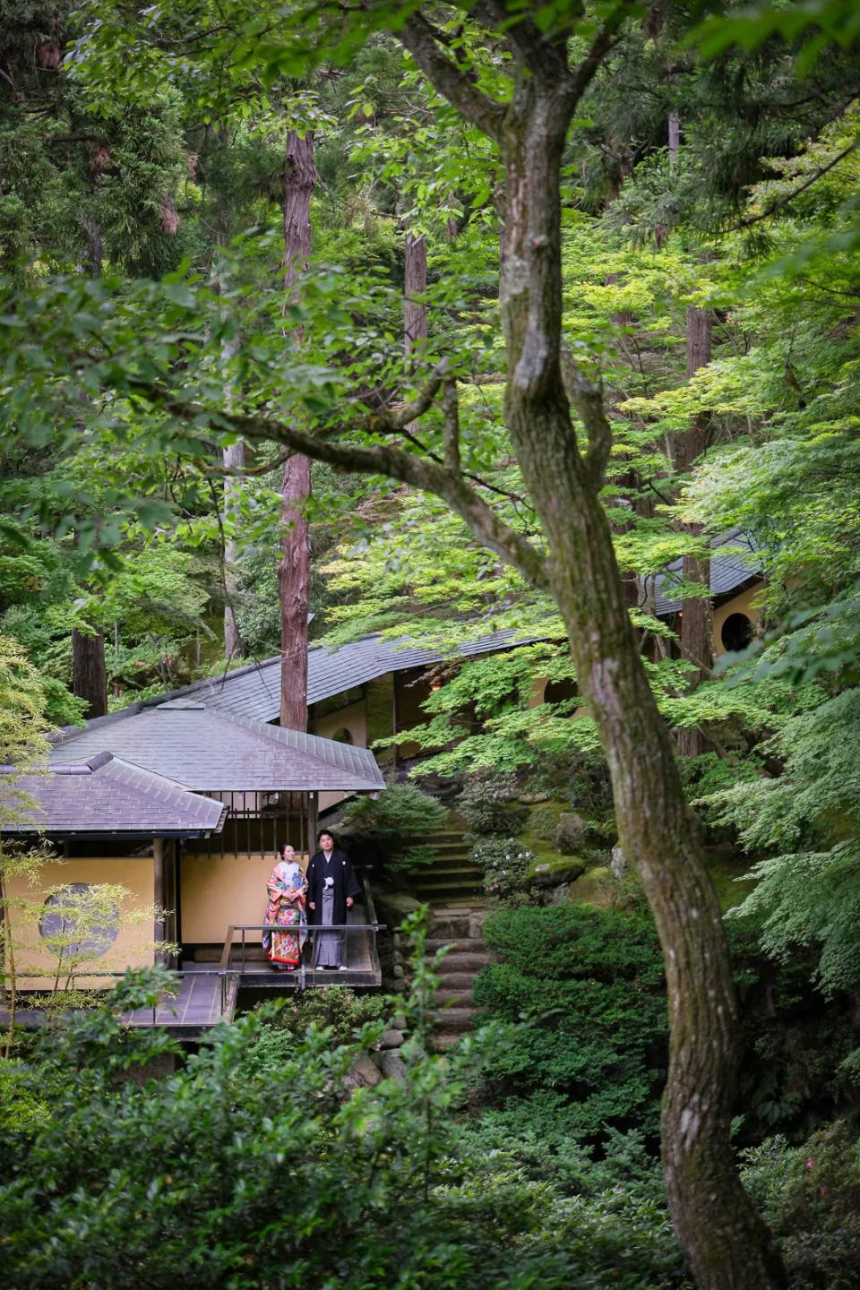 山中温泉の緑に囲まれた建物の前に立つ和装のふたり